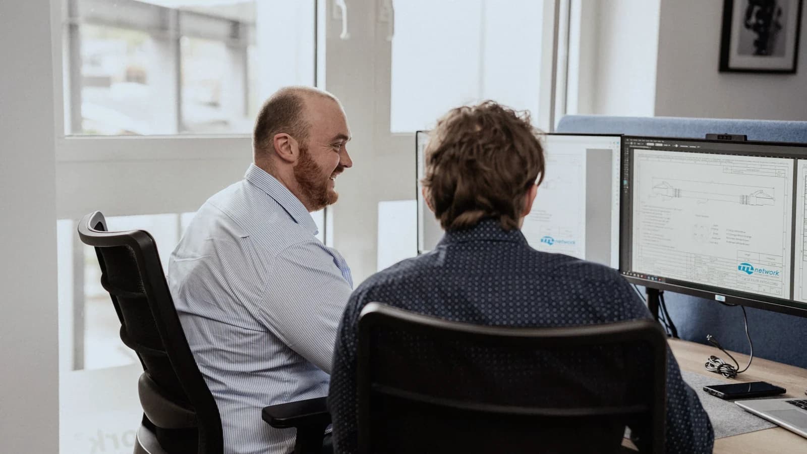 Two colleagues at a workstation with two monitors