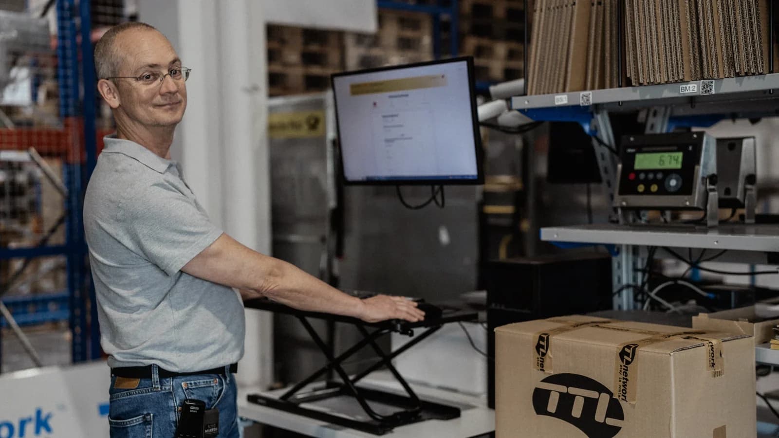 Employee at a height-adjustable packing station with a monitor and shipping box