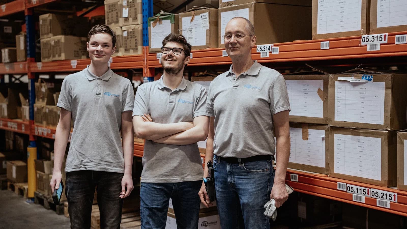 Three warehouse colleagues side by side in a racking aisle