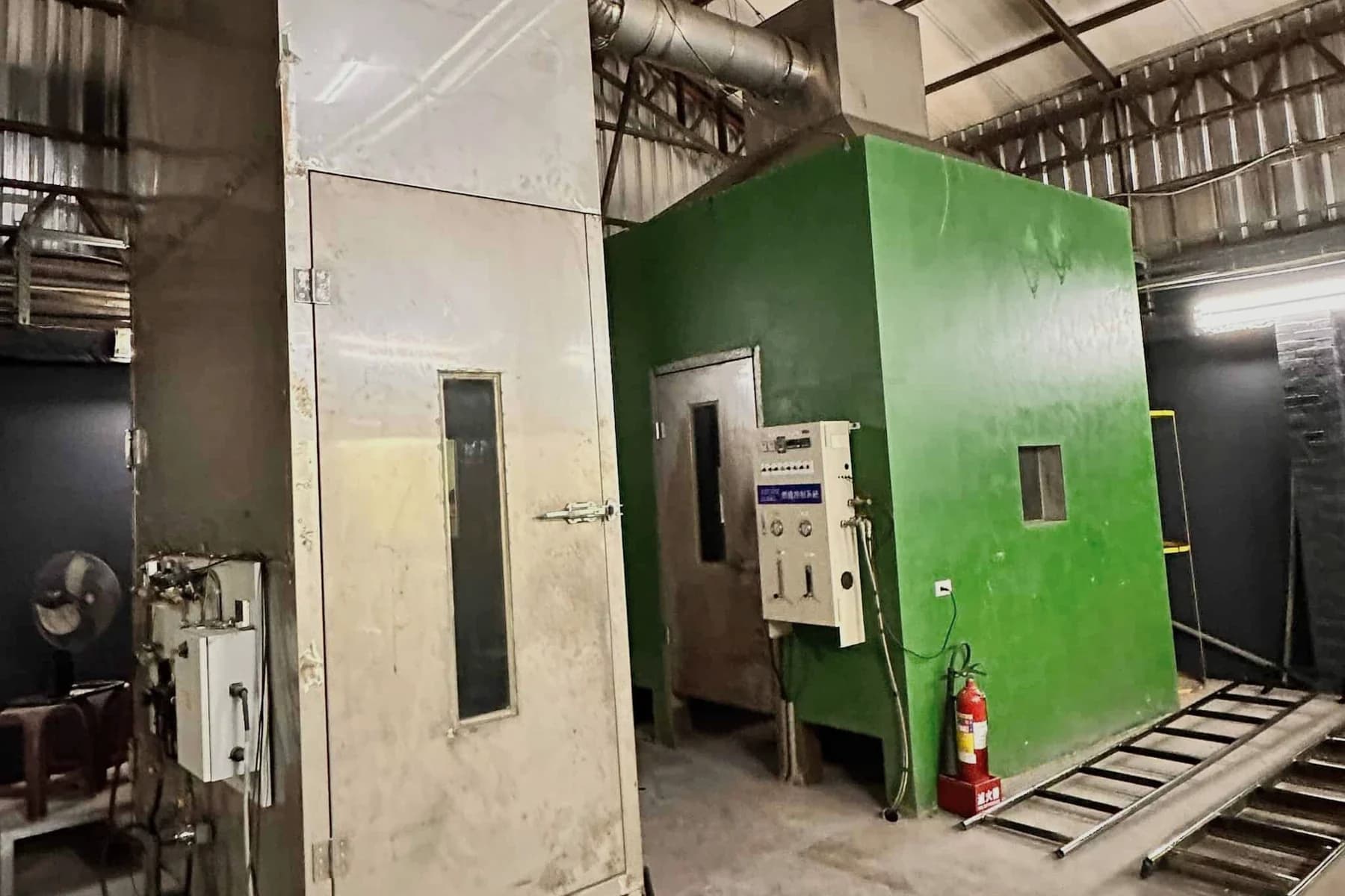 Two fire test chambers in a workshop, one in stainless steel, one painted green with a control panel and fire extinguisher