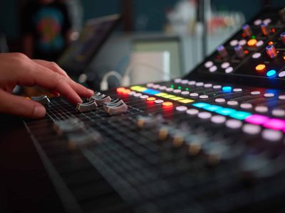 Close-up of a professional audio mixing console with glowing knobs and buttons in a recording studio.